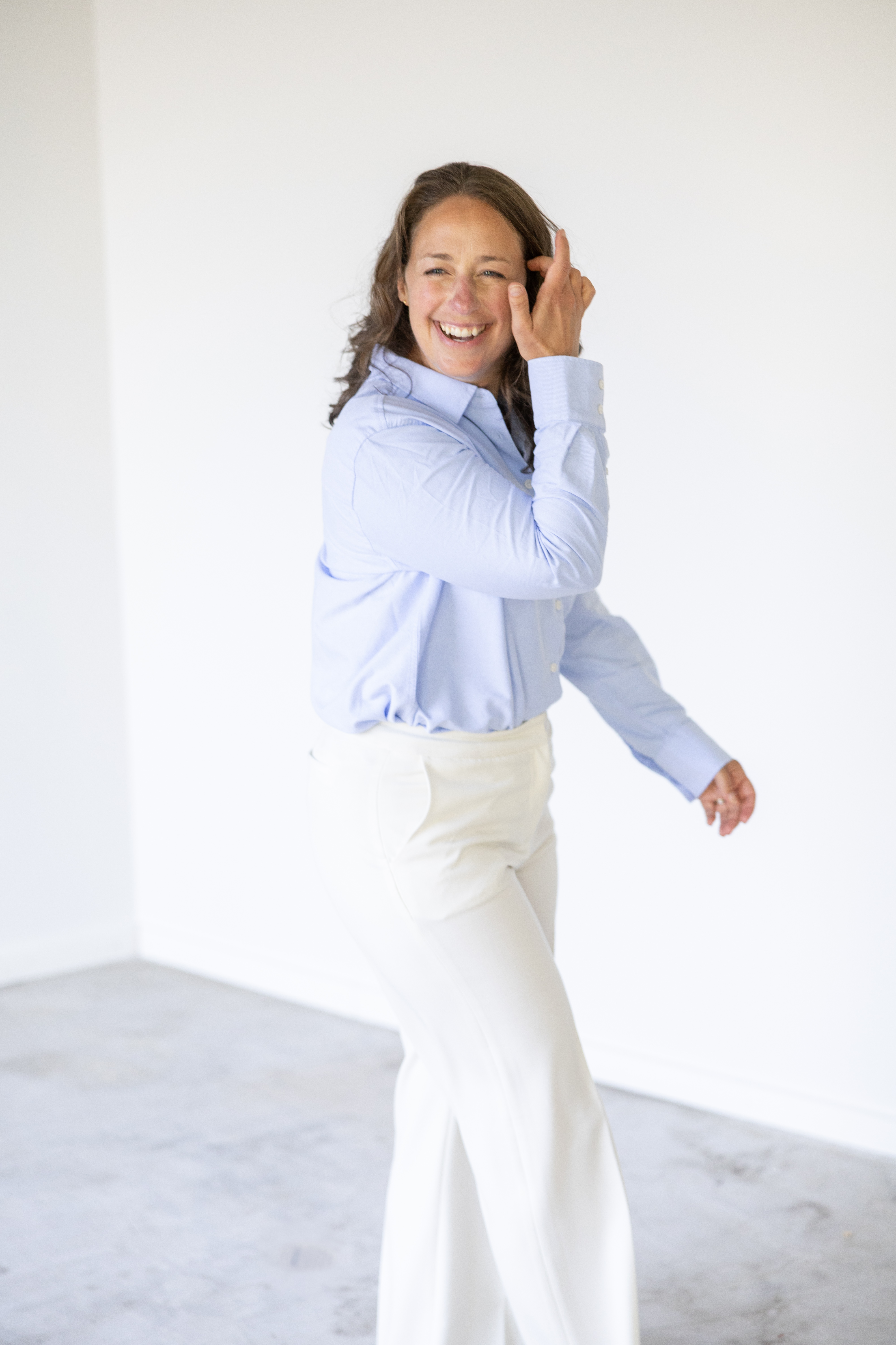 Liz smiling in a light blue shirt and white trousers in a bright studio