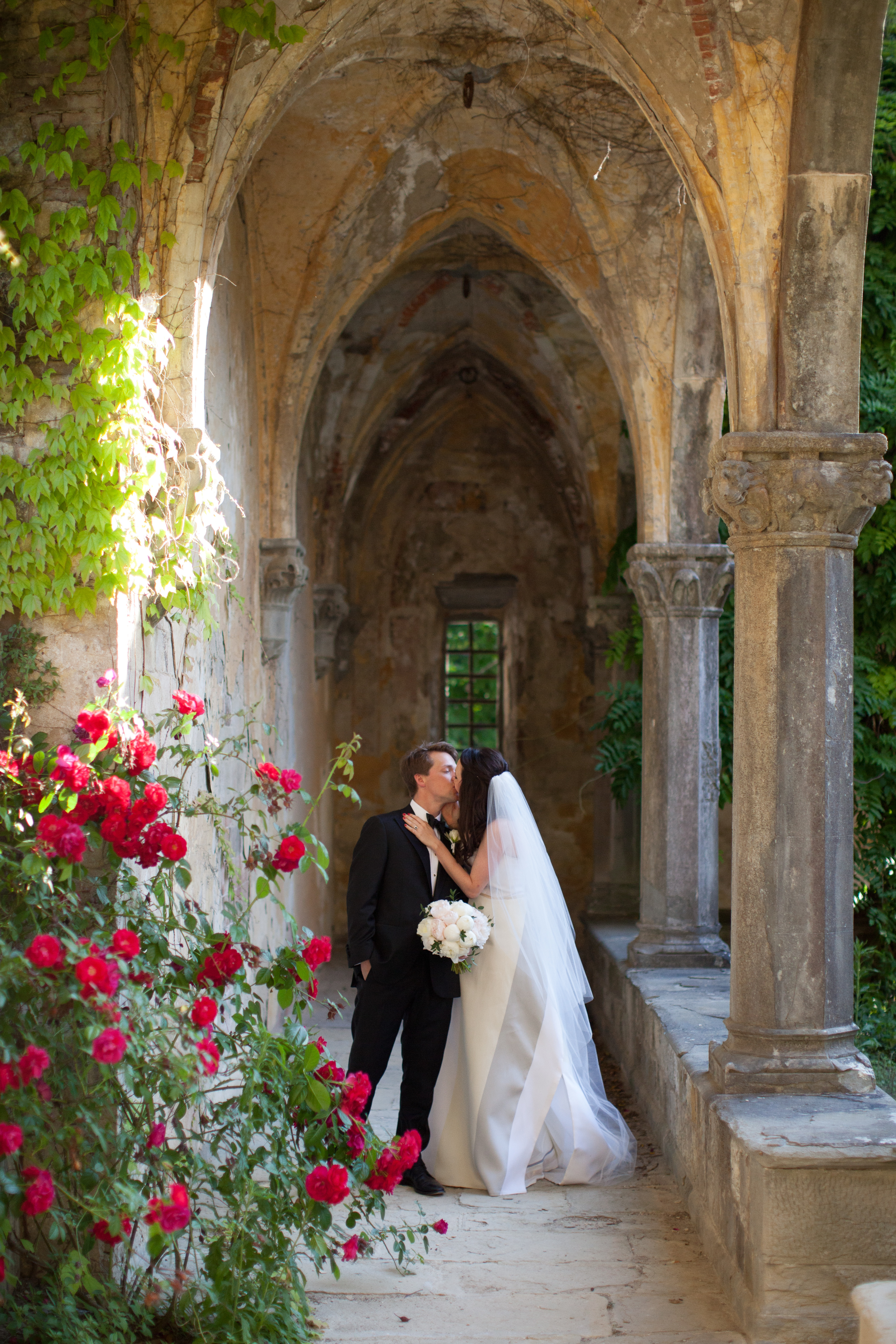 Bride and groom kissing in a stone archway with roses