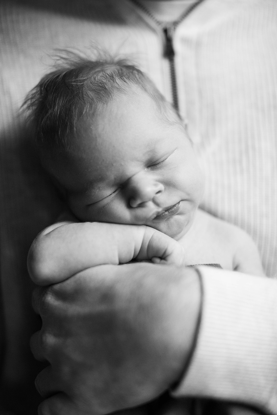 Sleeping newborn held close in black and white